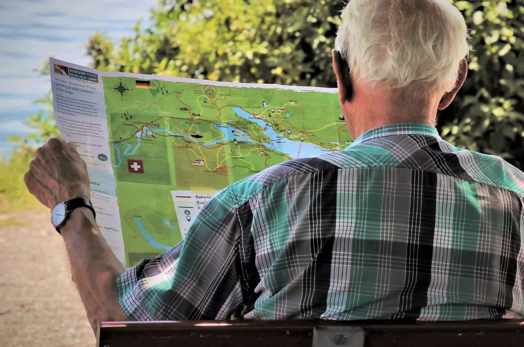 Old man sitting on a bench and looking at a city map.