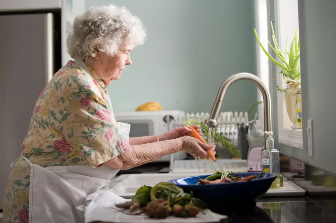 Senior woman washing vegetables in the kitchen sink.